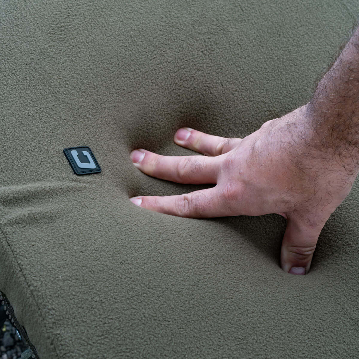 Hand pressing into soft fleece-covered memory foam topper for comfort while Carp Fishing.