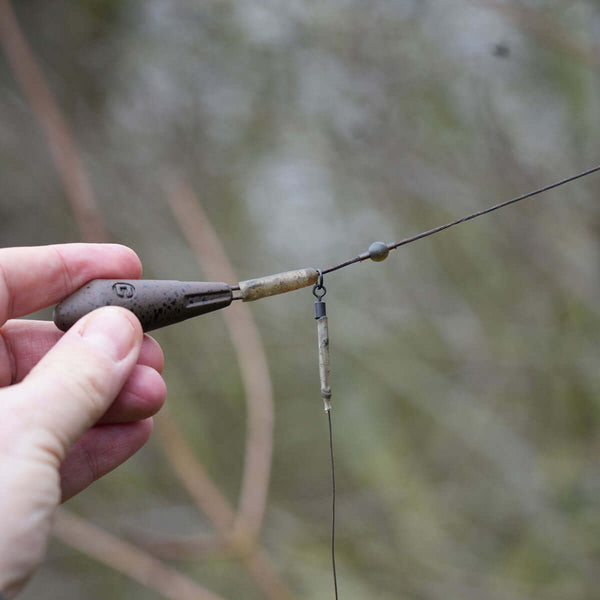 Hand holding a fishing rig with helicopter leadcore leaders and tackle components in a natural setting.